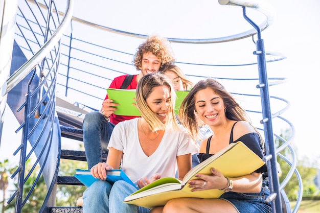 Damas estudiando en la escalera cerca de amigos