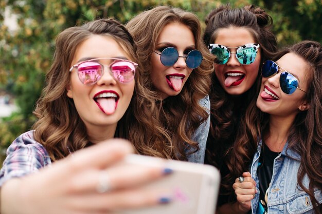 Damas de moda con peinado tomando selfie al aire libre.