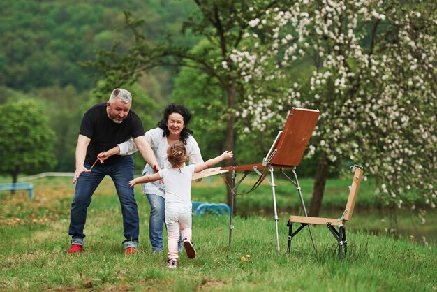 Dame un abrazo. La abuela y el abuelo se divierten al aire libre con su nieta. Concepción de la pintura