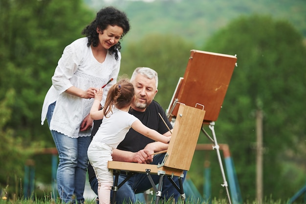 Dame ese cepillo. La abuela y el abuelo se divierten al aire libre con su nieta. Concepción de la pintura