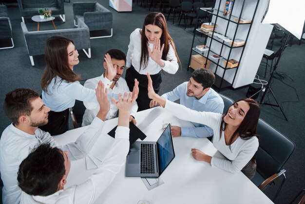 Dando choca esos cinco. Vista superior de los trabajadores de oficina en ropa clásica sentados cerca de la mesa usando una computadora portátil y documentos