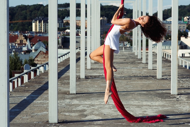 Danza aérea en la azotea, bailarina de seda morena sexy en vestido blanco