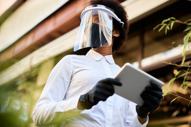 Foto gratuita debajo de la vista de la camarera afroamericana que usa una tableta digital mientras usa una máscara facial y una visera
