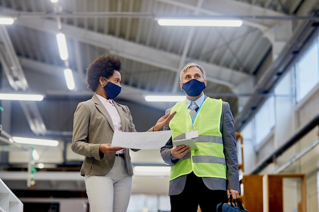 Debajo de la vista de una mujer de negocios negra hablando con un inspector de control de calidad que visita la fábrica durante la pandemia del coronavirus