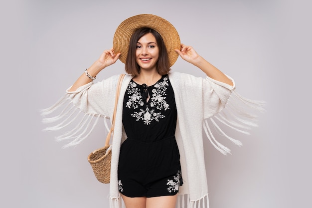 Debonair chica de ojos oscuros con sombrero de paja y traje de verano boho posando.