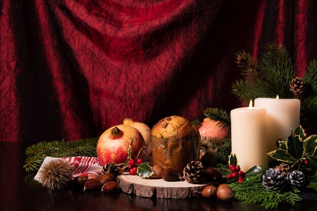 Decoración navideña con velas, rama de pino, conos, frutas y panettone.