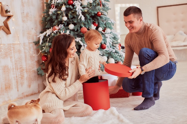 Decoraciones de vacaciones de invierno. Colores cálidos. Mamá, papá e hijita juegan con un perro.