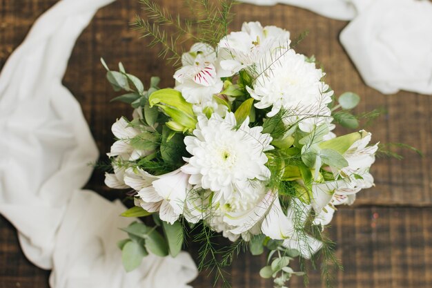 Decorativo ramo de flores blancas con bufanda en mesa de madera.