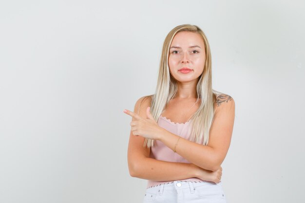 Dedo acusador femenino joven al lado en camiseta, minifalda y mirando confiado.