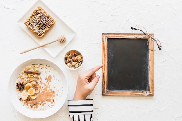 Dedo acusador femenino en la pequeña pizarra en blanco con desayuno saludable; panal y nueces