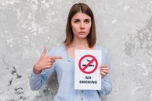 Foto gratuita dedo acusador de la mujer en el cartel de no fumadores de pie cerca de la pared degradado