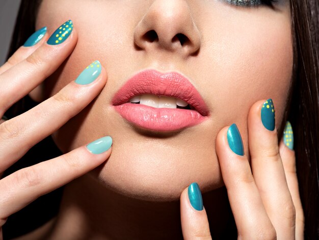Dedos de mujer con motton color azul de las uñas en la cara