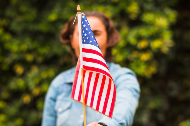 Defocused mujer sosteniendo la bandera estadounidense de Estados Unidos delante de su cara