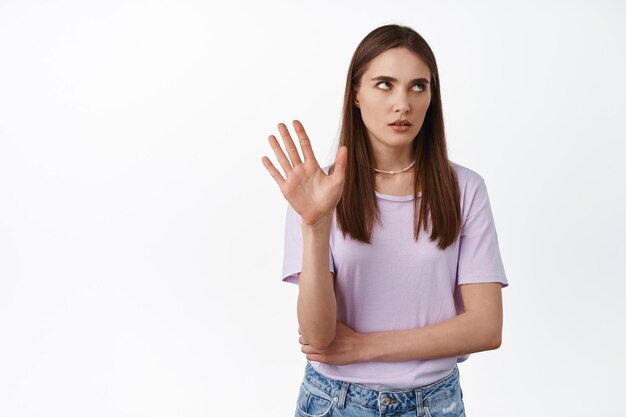 Deja de hablar. Bla, bla, que molesto. Joven mujer arrogante pone los ojos en blanco y levanta la mano para bloquear, negándose a escuchar, eso es suficiente, aburrida de la conversación, fondo blanco