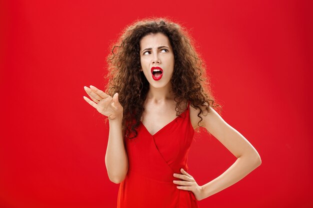 Deja de hablar de que me estás enfermando. Disgustada y arrogante mujer quisquillosa de cabello oscuro con peinado rizado que dice bla-blah alejándose de la persona molesta rodando los ojos hacia arriba y frunciendo el ceño por la aversión.