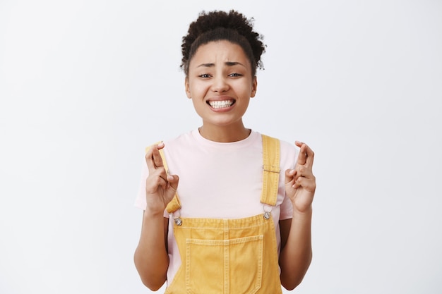 Deja que mi sueño se haga realidad. Intensa mujer afroamericana atractiva preocupada esperando un resultado importante, cruzando los dedos y apretando los dientes, suplicando milagros, esperando y rezando