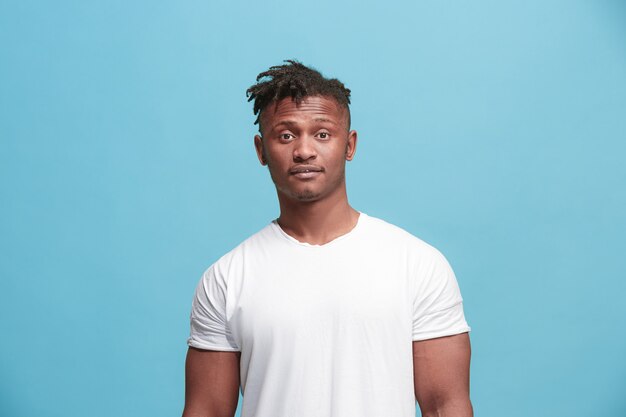 Deleite. Retrato delantero de medio cuerpo masculino afroamericano aislado en fondo de estudio azul. Joven, emocional, sonriente, sorprendido hombre de pie. Emociones humanas, concepto de expresión facial. Colores de moda