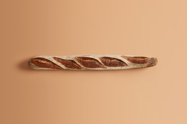 Deliciosa baguette crujiente francesa tradicional horneada por un profesional, lista para ser consumida, aislada sobre fondo beige. Producto de masa madre orgánica. Cocina casera, panadería, concepto de comida natural.