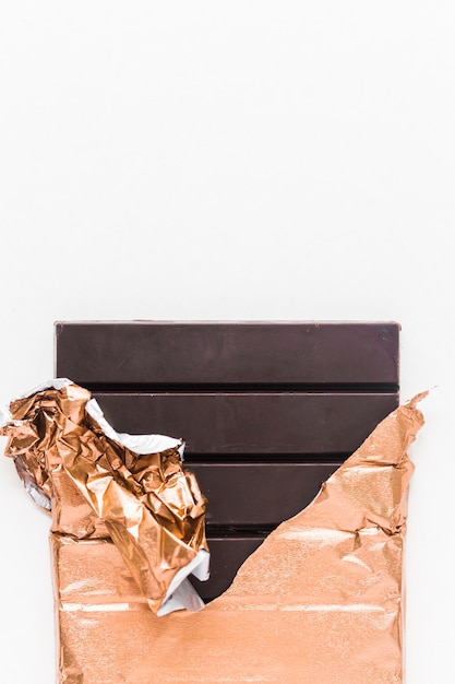 Deliciosa barra de chocolate envuelta en papel dorado sobre fondo blanco