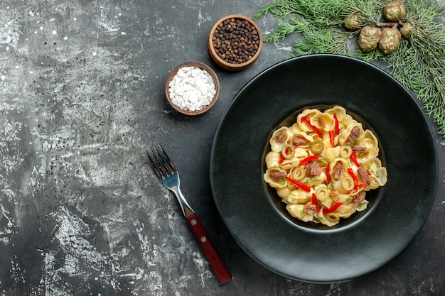 Deliciosa conchiglie con verduras y verduras en un plato y cuchillo y diferentes especias sobre fondo gris