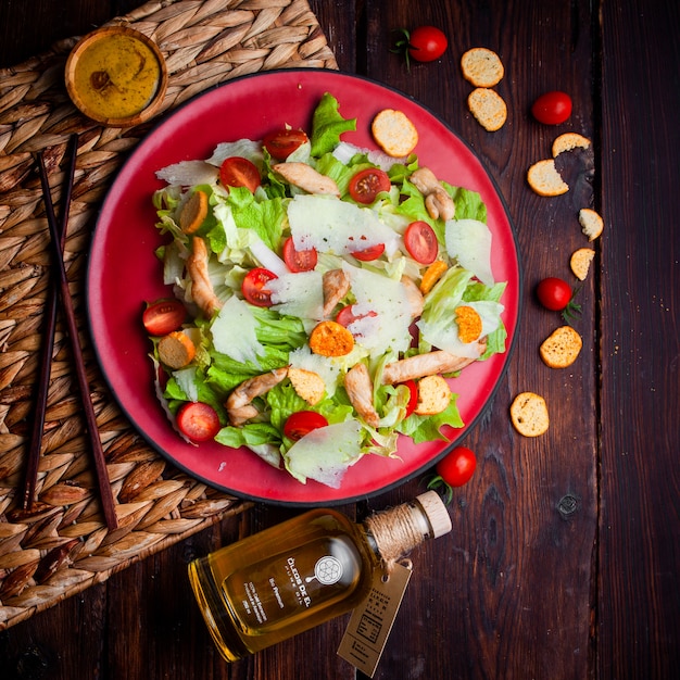 Deliciosa ensalada en un plato rojo con aceite sobre fondo de madera, endecha plana.