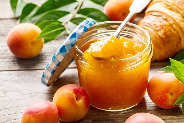 Deliciosa fruta naranja de albaricoque atasco en frasco de vidrio con frutas en la mesa de madera. De cerca.