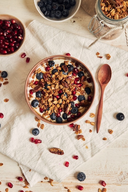 Deliciosa granola vegana saludable con nueces pecanas en un tazón de frutas con yogur sobre una mesa blanca