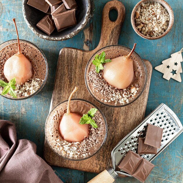 Deliciosa mousse de chocolate con peras pochadas en marcos de vidrio sobre una mesa cuadrada de madera azul