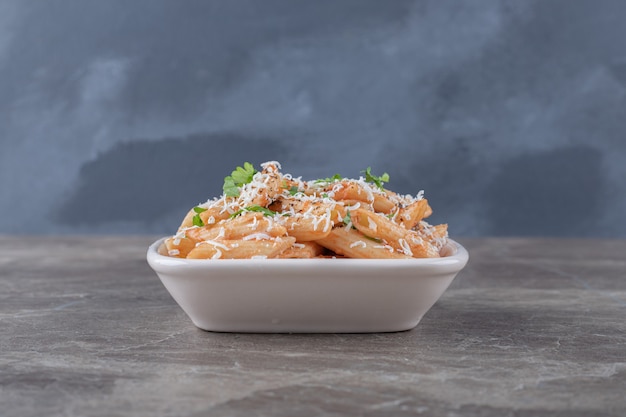 Deliciosa pasta penne en el bol, sobre la superficie de mármol.