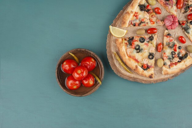 Deliciosa pizza caliente y tazón de fuente de tomates en escabeche en el cuadro azul.