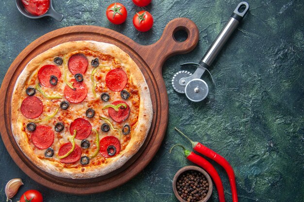 Deliciosa pizza casera en la tabla de cortar de madera y tomates, ajo, ketchup, pimienta sobre una superficie oscura aislada