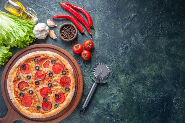 Deliciosa pizza casera en la tabla de cortar de madera tomates ketchup ajo pimienta aceite botella paquete verde sobre superficie oscura