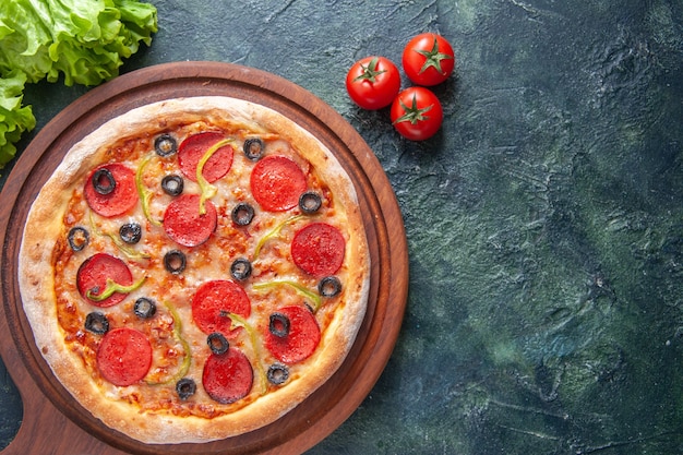 Deliciosa pizza casera en la tabla de cortar de madera, tomates, salsa de tomate, paquete verde sobre superficie oscura