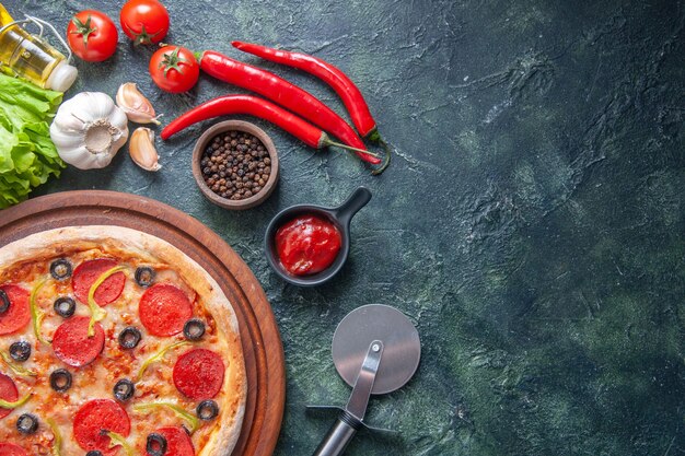 Deliciosa pizza casera en tablero de madera tomates ketchup ajo pimienta aceite botella paquete verde sobre superficie oscura en primer plano