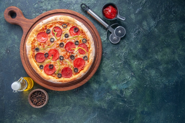 Deliciosa pizza casera en tomates de tablero de madera y salsa de tomate de pimienta de botella de aceite en el lado derecho sobre una superficie oscura