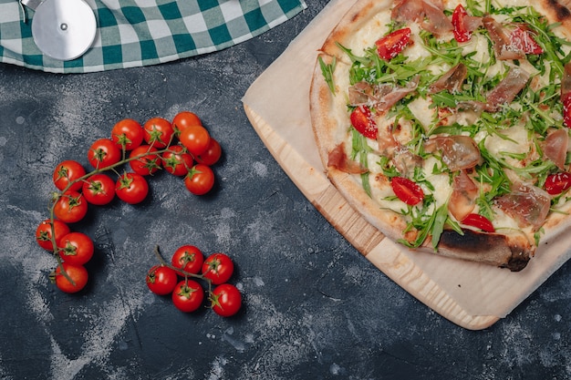 Deliciosa pizza napolitana a bordo con tomates cherry, espacio libre para texto