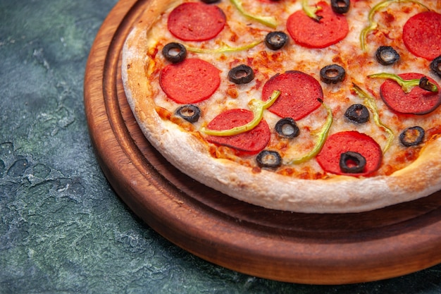 Deliciosa pizza en la tabla de cortar de madera en el lado izquierdo sobre una superficie oscura aislada con espacio libre en primer plano