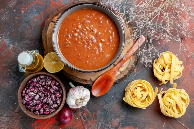 Deliciosa sopa para cenar con una cuchara y limón en una bandeja de madera, frijoles, ajo, cebolla y otros productos en la mesa de colores mezclados