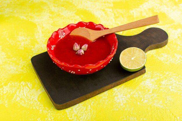Deliciosa sopa de tomate dentro de la placa roja con una rodaja de limón sobre amarillo, comida de sopa cena comida vegetal