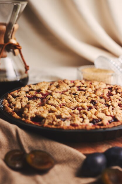 Deliciosa tarta de ciruela con café Chemex e ingredientes con tela sobre una mesa de madera con tela