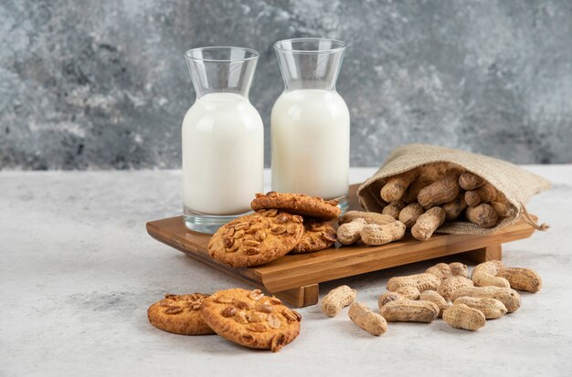 Deliciosas galletas con cacahuetes orgánicos y miel con vaso de leche sobre tabla de madera.