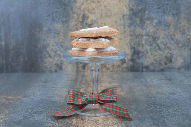 Deliciosas galletas de Navidad en placa de vidrio con arco sobre mesa de mármol.