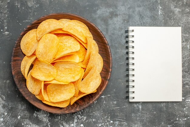 Deliciosas papas fritas caseras en una placa marrón y un cuaderno sobre una mesa gris