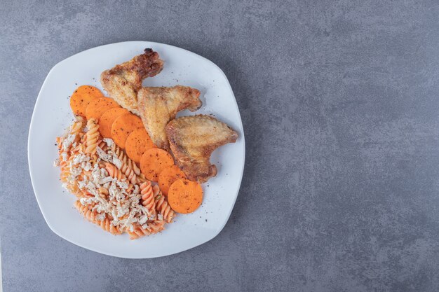 Deliciosas pastas fusilli y alitas de pollo en un plato blanco.