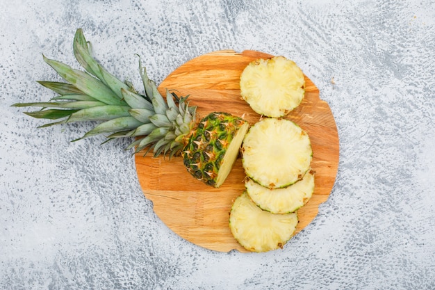 Deliciosas rodajas de piña en una tabla de cortar redonda en la superficie del grunge, vista desde arriba.