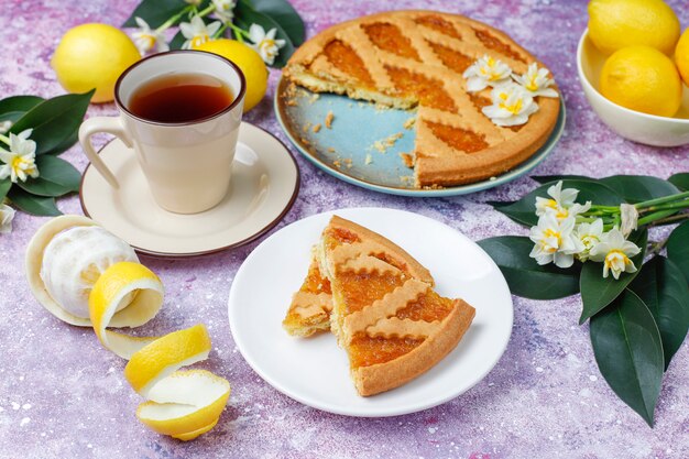 Deliciosas rodajas de tarta de limón con limones frescos y una taza de té, vista superior