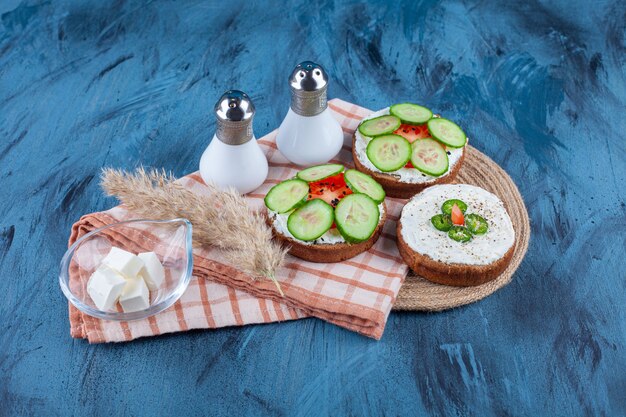 Deliciosas tostadas con crema y pepinos en rodajas sobre superficie azul.