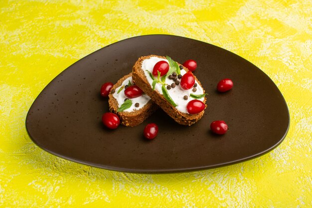 Deliciosas tostadas de pan con crema agria y cornejos dentro de la placa marrón sobre amarillo