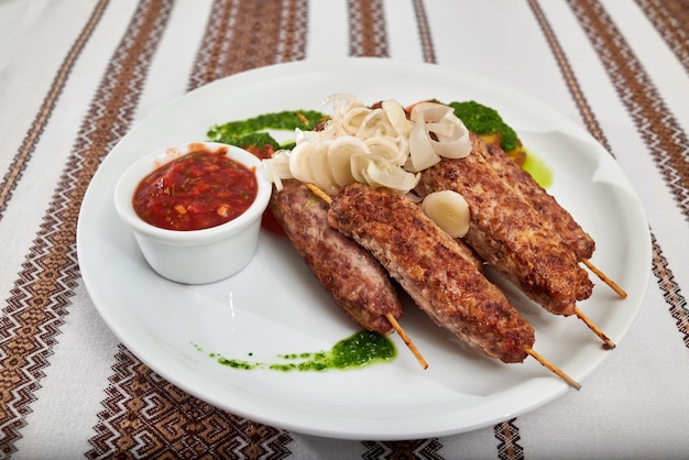 Foto gratuita delicioso aperitivo de restaurante para cerveza y alcohol fuerte: salchicha asada con tomate y salsa verde y rodajas de cebolla. una mesa está cubierta con un mantel bordado.