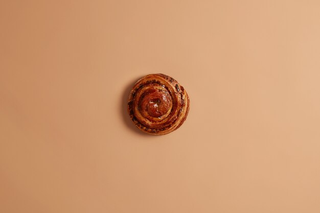 Delicioso bollo de canela en forma de remolino recién horneado para su merienda o desayuno. Apetitoso pastel de hojaldre insalubre sobre fondo beige. Concepto de repostería y panadería. Rollo francés entero delicioso